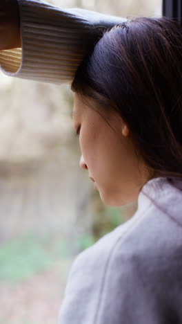 Vertical-Video-Close-Up-Of-Stressed-Or-Anxious-Woman-Suffering-With-Depression-Anxiety-Loneliness-Or-Agoraphobia-Leaning-Against-Window-At-Home